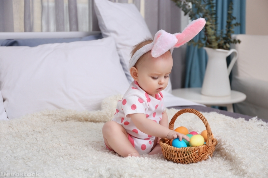 Devostock Cute funny baby with bunny ears and basket full of Easter eggs a